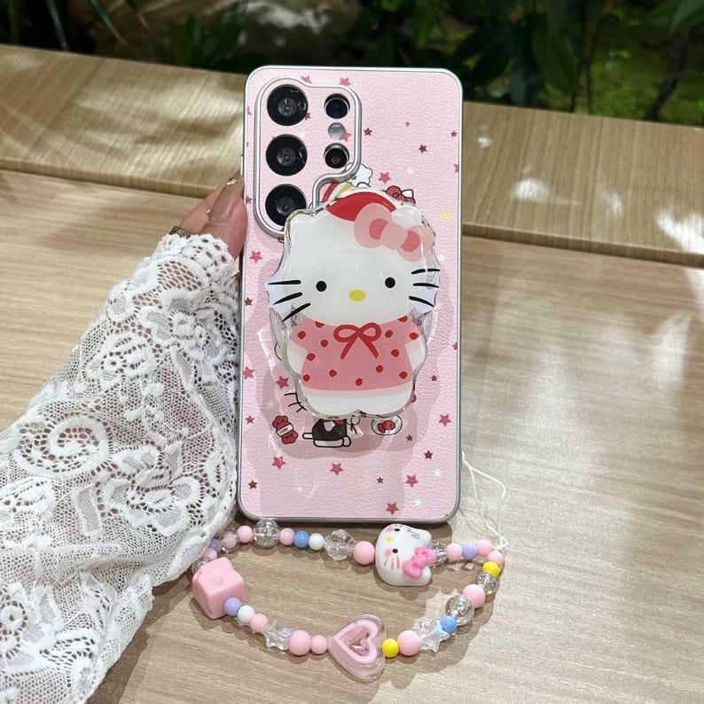 Peut inclure: Coque de t&eacute;l&eacute;phone rose avec un motif Hello Kitty, accompagn&eacute;e d'un bracelet assorti. L'&eacute;tui pr&eacute;sente un motif d'&eacute;toiles et une figurine Hello Kitty en 3D. Le bracelet comprend des perles roses, bleues et transparentes, avec un charm Hello Kitty et un charm c&oelig;ur rose.