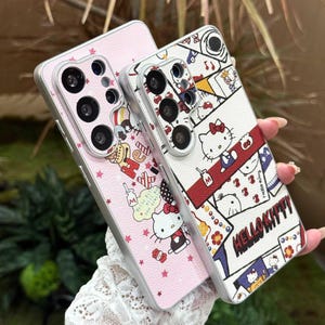 Peut inclure: Deux coques de t&eacute;l&eacute;phone avec des motifs Hello Kitty. L'une est rose avec un motif d'&eacute;toiles r&eacute;p&eacute;t&eacute;es et des graphiques Hello Kitty. L'autre est blanche avec un motif de collage Hello Kitty, avec le texte "Hello Kitty". Les deux coques ont des bords argent&eacute;s.