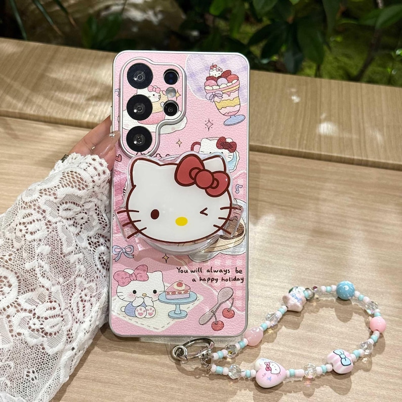 May include: Pink phone case featuring a Hello Kitty design with a red bow, desserts, and the text "You will always be a happy holiday." Includes a beaded wrist strap with pink, blue, and clear beads.