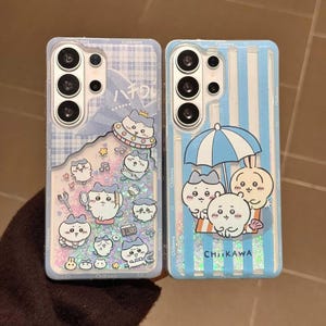 以下が含まれることがあります： キュートな漫画のキャラクターデザインの携帯電話ケース2つ。1つのケースは、浮遊する星と音符のある青と白のチェック柄です。もう1つのケースは、傘の下に漫画のキャラクターがいる青と白のストライプです。