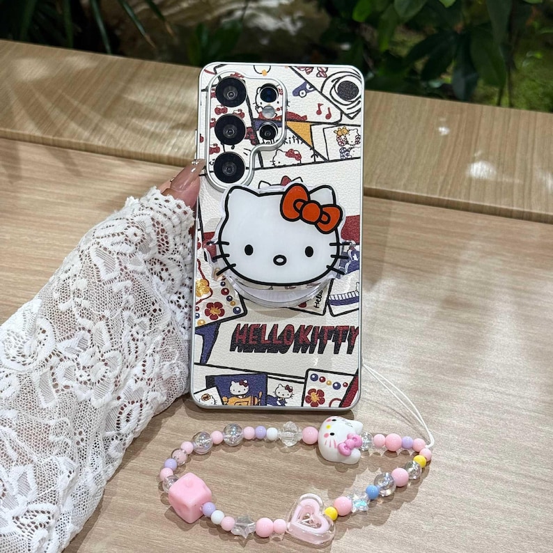 Peut inclure: Une coque de t&eacute;l&eacute;phone Hello Kitty avec une poign&eacute;e pop-up et un bracelet de perles assorti. L'&eacute;tui pr&eacute;sente un fond blanc avec des illustrations color&eacute;es et le personnage Hello Kitty. Le bracelet a des perles roses, violettes et transparentes avec un charme Hello Kitty.