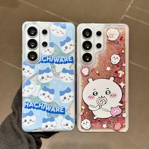 以下が含まれることがあります： 2つの透明な携帯電話ケース。1つのケースは、漫画の猫の顔と「Hachiware」と「Chiware」の文字が入った青色の背景です。もう1つのケースは、漫画のキャラクターと「Chiikawa」の文字が入ったピンクのグリッターの背景です。