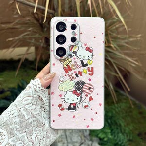 Peut inclure: Coque de t&eacute;l&eacute;phone rose avec des graphismes Hello Kitty. L'&eacute;tui pr&eacute;sente un motif d'&eacute;toiles r&eacute;p&eacute;t&eacute;es et les mots "Hello Kitty" dans un design color&eacute;. L'&eacute;tui pr&eacute;sente &eacute;galement une image de dessin anim&eacute; de Hello Kitty tenant des ballons.