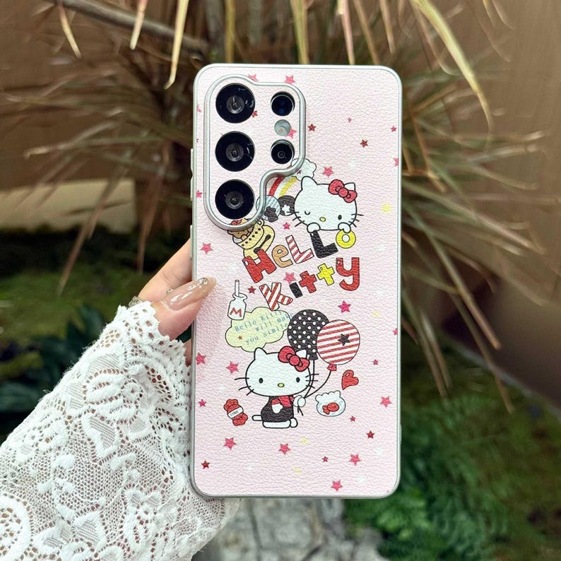 Peut inclure: Coque de t&eacute;l&eacute;phone rose avec des graphismes Hello Kitty. L'&eacute;tui pr&eacute;sente un motif d'&eacute;toiles r&eacute;p&eacute;t&eacute;es et les mots "Hello Kitty" dans un design color&eacute;. L'&eacute;tui pr&eacute;sente &eacute;galement une image de dessin anim&eacute; de Hello Kitty tenant des ballons.