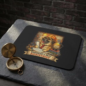 Könnte beinhalten: Schwarzes rechteckiges Mousepad mit einem Cartoon-Hund mit Schutzhelm und Krawatte, mit dem Text "ENGINEER'S BEST ASSISTANT". Das Design umfasst technische Werkzeuge und Bücher. Ein antiker Messingkompass befindet sich im Vordergrund.