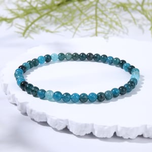 May include: A circular beaded bracelet featuring small, polished spherical stones in varying shades of blue, ranging from deep teal and dark navy to lighter sky blue and turquoise, arranged in a continuous, uniform strand of smooth, round beads.