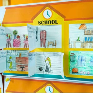 May include: A child's artwork depicting a school scene with classrooms and activities. The image includes the word "SCHOOL" and handwritten text. The drawings are set against an orange and yellow background, with a clock and various drawings.