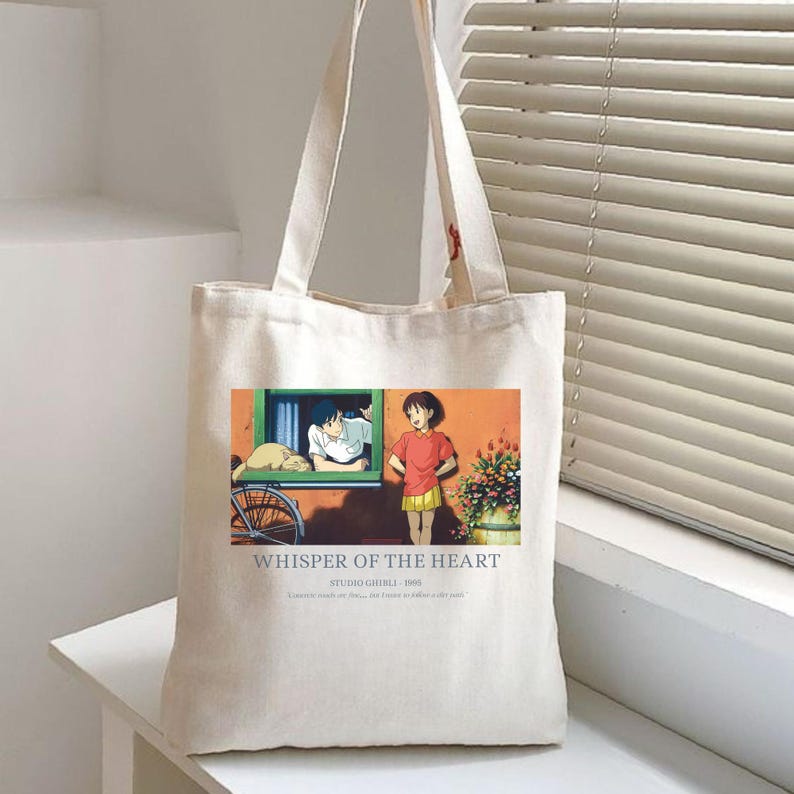 May include: Off-white canvas tote bag featuring a colorful anime scene from "Whisper of the Heart." The image shows two characters, a boy and a girl, with text that reads "Whisper of the Heart" and "Studio Ghibli 1995."