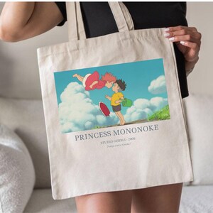 May include: Beige tote bag featuring a colorful illustration from the animated film "Princess Mononoke." The image shows two characters, one in a red dress and the other in a yellow shirt, with the text "PRINCESS MONONOKE" below the image.