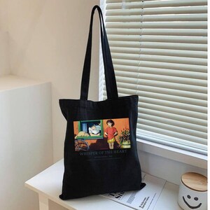 May include: Black tote bag with long handles. The bag features a colorful graphic from "Whisper of the Heart" with a boy and girl. The text "Whisper of the Heart" is printed below the graphic.