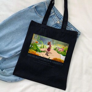 K&ouml;nnte beinhalten: Schwarze Tragetasche mit einer farbenfrohen Illustration aus "Arrietty &ndash; Die wundersame Welt der Borger". Das Bild zeigt ein M&auml;dchen, das auf einer riesigen Hand in einem Garten steht. Der Text "THE SECRET WORLD OF ARRIETTY" ist darunter gedruckt. Die Tasche hat schwarze Griffe.