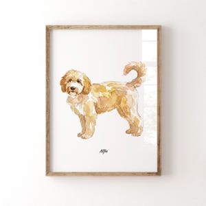 Könnte beinhalten: Ein gerahmtes Aquarellbild eines goldbraunen Doodle-Hundes, der im Profil nach links schaut und den Schwanz nach oben gebogen hat. Das Kunstwerk ist auf weißem Hintergrund dargestellt und zeigt den Namen Alfie in schwarzer Schrift unter dem Hund.