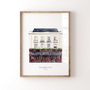 May include: A watercolor print in a wooden frame depicting The Builders Arms in Chelsea. The building features a cream-colored upper facade with four windows and a dark red ground floor with an awning. The text reads The Builders Arms Chelsea.