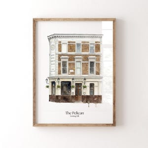 Può includere: Stampa ad acquerello incorniciata del pub The Pelican a Notting Hill, Londra. L'edificio è marrone e bianco con un'insegna che elenca birra, vino, liquori e cibo. Il nome e la posizione del pub sono stampati in basso.