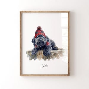 Op de afbeelding: Waterverfprint van een zwarte hond met een rood-zwarte geruite muts en sjaal. De hond ligt op een stenen oppervlak. De naam "Charlie" staat eronder in cursief geschreven.