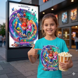 May include: A young girl points to a teal t-shirt featuring a colorful graphic from "The Super Mario Bros. Movie." The design includes Mario, Luigi, Princess Peach, and Bowser. She holds a popcorn container in front of a movie poster.