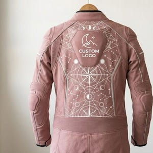 Upper back view of a pink female leather riding suit showing a detailed, white abstract geometric print. The intricate design includes a compass star, moon phases, and a custom logo on the upper back panel, completely free of pockets for a smooth finish.