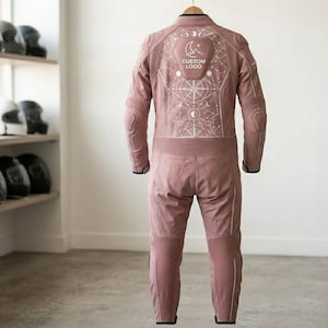 Full-length rear view of a women's pink cowhide leather one-piece bike racing suit hanging in a showroom. The suit showcases a clean minimalist silhouette without back pockets, detailed cosmic line-art on the back, accordion stretch panels at the waist, and protective leg padding.