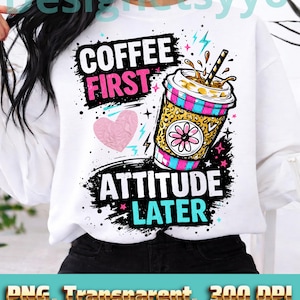 以下が含まれることがあります： 「COFFEE FIRST ATTITUDE LATER」の文字が入った白いスウェットシャツ。デザインには、ヒョウ柄、ピンクと青のストライプ、花が描かれたコーヒーカップが含まれています。ピンクのハートと稲妻も特徴です。