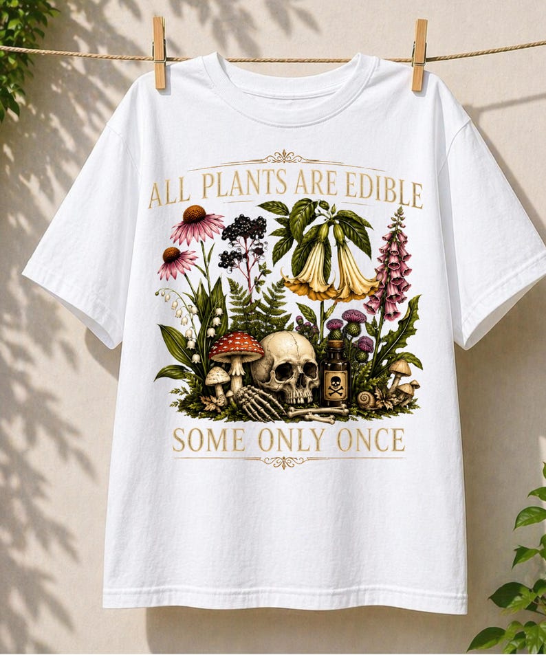 May include: White t-shirt with a botanical illustration featuring flowers, mushrooms, a skull, and a poison bottle. The text "ALL PLANTS ARE EDIBLE" and "SOME ONLY ONCE" are printed in gold.