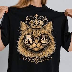 May include: Black t-shirt featuring a detailed illustration of a cat wearing a crown and round glasses. The glasses display the text "THIS IS AN OUT RAGE!". The cat is golden-brown with ornate decorative elements.