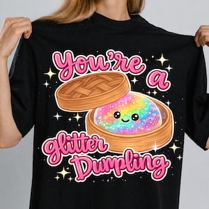 Puede incluir: Camiseta negra con un diseño de dumpling de dibujos animados. El dumpling tiene un relleno de purpurina arcoíris y una cara sonriente. La inscripción rosa dice "You're a Glitter Dumpling" encima y debajo de la imagen.