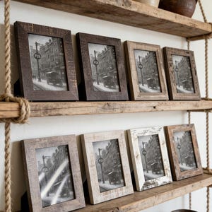 May include: A collection of framed pictures displayed on rustic wooden shelves. The frames are various shades of brown and white, with a distressed finish. Each frame holds a black and white image of a street scene with a pub sign.