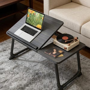 May include: A dark gray laptop table with a black metal frame. A laptop with a floral screen saver sits on the angled top. A vintage record player and vinyl records are on the lower level. The table is on a gray shag rug.