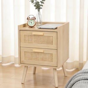 May include: A light wood nightstand with two drawers featuring woven cane panels. The nightstand has a top shelf with a small alarm clock, a laptop, and a glass vase with greenery. The nightstand is supported by four angled legs.