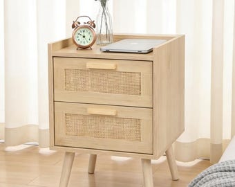 May include: A light wood nightstand with two drawers featuring woven cane panels. The nightstand has a top shelf with a small alarm clock, a laptop, and a glass vase with greenery. The nightstand is supported by four angled legs.