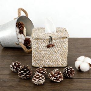 May include: A woven tissue box with a wooden toggle closure, surrounded by pine cones and a cotton ball. A galvanized metal bucket with a rope handle is filled with cotton and pine cones. The items are arranged on a dark wood surface.