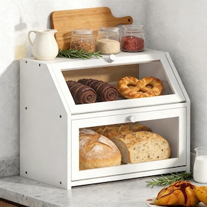 May include: A white wooden bread box with a glass front, displaying various baked goods like bread and pastries. The top shelf holds jars of spices and a small pitcher. A wooden cutting board is also visible.