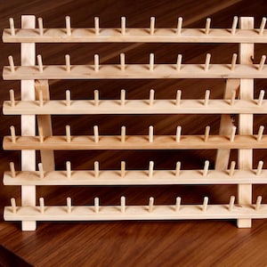 May include: A wooden thread spool holder with multiple rows of pegs. The natural wood color and simple design make it a functional and decorative item for sewing enthusiasts. The holder is designed to organize spools of thread.