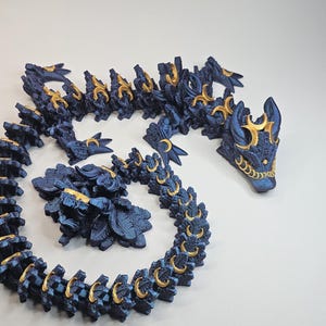 Könnte beinhalten: Eine dunkelblaue, bewegliche Drachenfigur mit goldenen Akzenten. Der Drache ist aufgerollt, Kopf und Schwanz sind sichtbar. Details umfassen Schuppen und dekorative Elemente. Die Figur besteht aus einem festen Material.