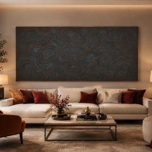 May include: A large rectangular wall art piece featuring a dark charcoal grey surface with raised, swirling copper-toned lines that create a topographic, abstract pattern. The artwork is mounted horizontally above a cream-coloured sectional sofa.
