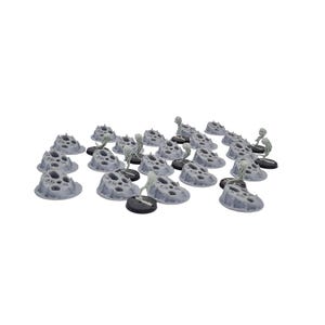 Puede incluir: Una colección de piezas de terreno grises en miniatura, cada una con una textura porosa similar a la roca. Pequeñas figuras esqueléticas se alzan sobre el terreno, montadas sobre bases negras. La escena sugiere un entorno de juego de mesa.