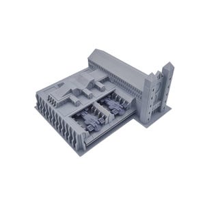 Può includere: Modello grigio stampato in 3D di un edificio dal design complesso. Il modello presenta più livelli, elementi architettonici dettagliati e veicoli in miniatura all'interno. L'estetica generale è futuristica e industriale.