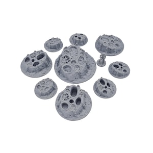 以下が含まれることがあります： テーブルゲーム用の、灰色で多孔質の岩のような地形パーツのコレクション。セットにはさまざまなサイズと形状が含まれており、近くに小さなフィギュアがあり、スケールを示唆しています。SFやファンタジーの世界に最適です。