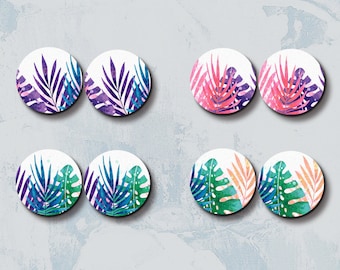 Op de afbeelding: Vier paar ronde houten oorbellen met aquarel tropische bladmotieven. De bladeren zijn in tinten paars, roze, teal, groen en oranje. De tekst "HALOCOLOR Professional Laser Cut Wood Charm" en websiteadres staan bovenaan en onderaan.