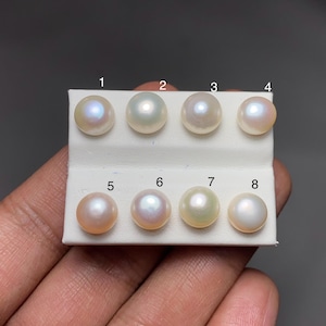 May include: Eight lustrous, round pearls of varying colors are displayed on a white card. The pearls range from white to peach, with iridescent overtones. The pearls are numbered 1 through 8.