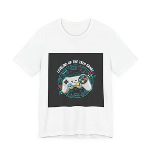 May include: White t-shirt featuring a graphic of a video game controller with the text "Leveling Up The Tech Game!". The controller is white with colorful buttons and neon green, blue, and pink accents. The design is on a black square.
