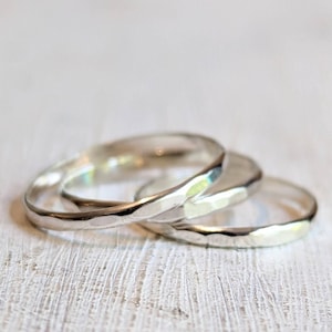 May include: A set of three thin, silver-colored metal rings with a hammered, textured surface. The rings are stacked and overlapping, showing a reflective, metallic finish with subtle indentations across the outer bands of each individual ring.