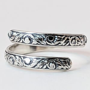 May include: A silver ring with a delicate, intricate design of swirling leaves and flowers. The ring is made of two bands that wrap around the finger.