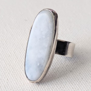 May include: A silver ring with a large oval-shaped white gemstone. The ring is set in a simple band.