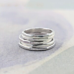 May include: A stack of three silver rings, each featuring a distinct hammered texture that creates a series of small, reflective facets along the outer surface of the metal bands. The rings are positioned one on top of the other in a vertical column.