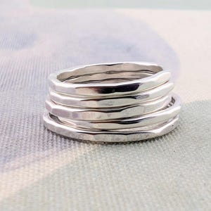 May include: A stack of five silver-colored rings with a hammered, textured finish. Each ring features a slightly irregular, organic shape with a polished, reflective surface. The rings are stacked neatly on top of one another in a vertical column.