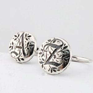 May include: Two silver rings with engraved initials. One ring features the letter "A" and the other the letter "Z", both surrounded by a floral design. The rings are set against a white background.