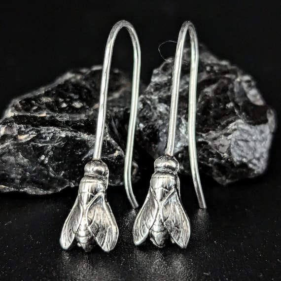 Hand-fabricated sterling silver fly earrings with genuine metalwork detail — hyper-specific entomology chic that most jewelers would never attempt.
