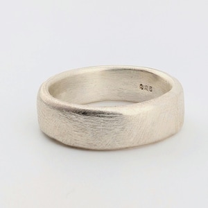 May include: A silver-colored ring with a brushed, textured finish on the exterior surface. The interior of the band features a clear hallmark stamp that reads 925, indicating the metal content. The ring has a wide, solid band design.