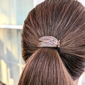 May include: A brown hair tie with a gold-toned cicada design.